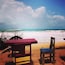 A beach with a wooden table and chair, a sandy shore, and the ocean in the background.