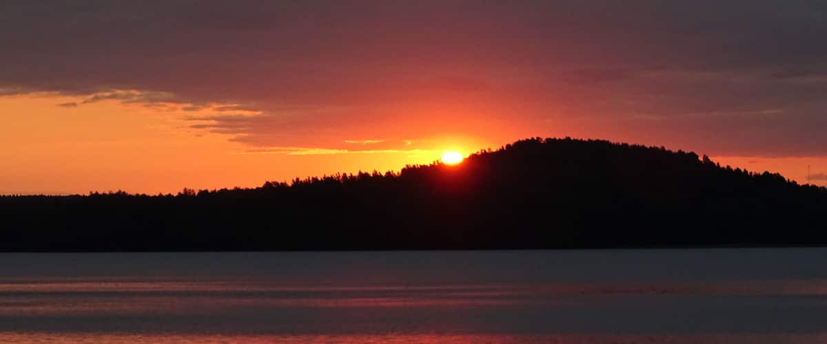 A sunset over a calm lake with a silhouette of a hill in the distance.