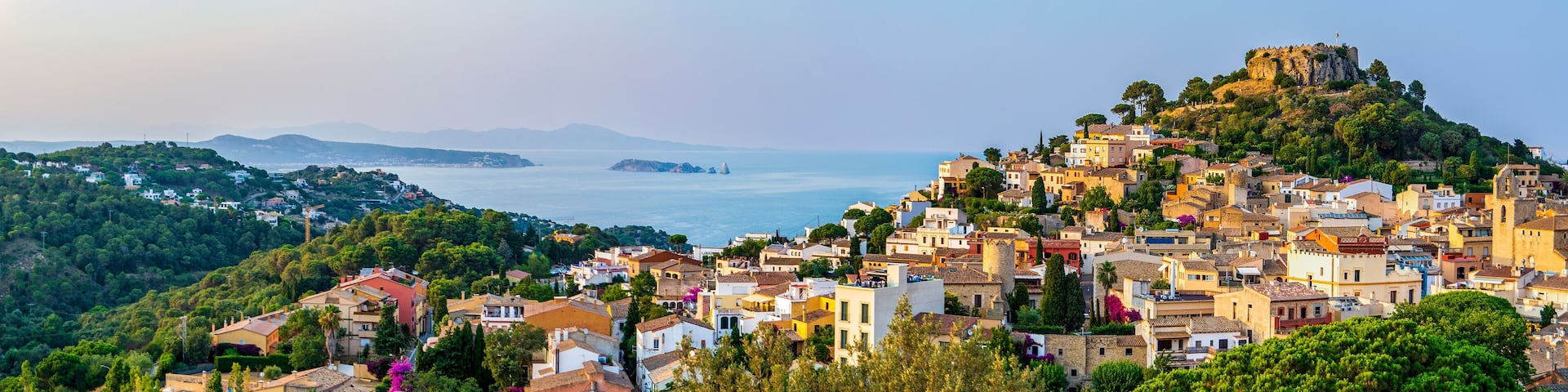 A coastal town with a prominent hilltop castle, dense greenery, and a view of the sea.