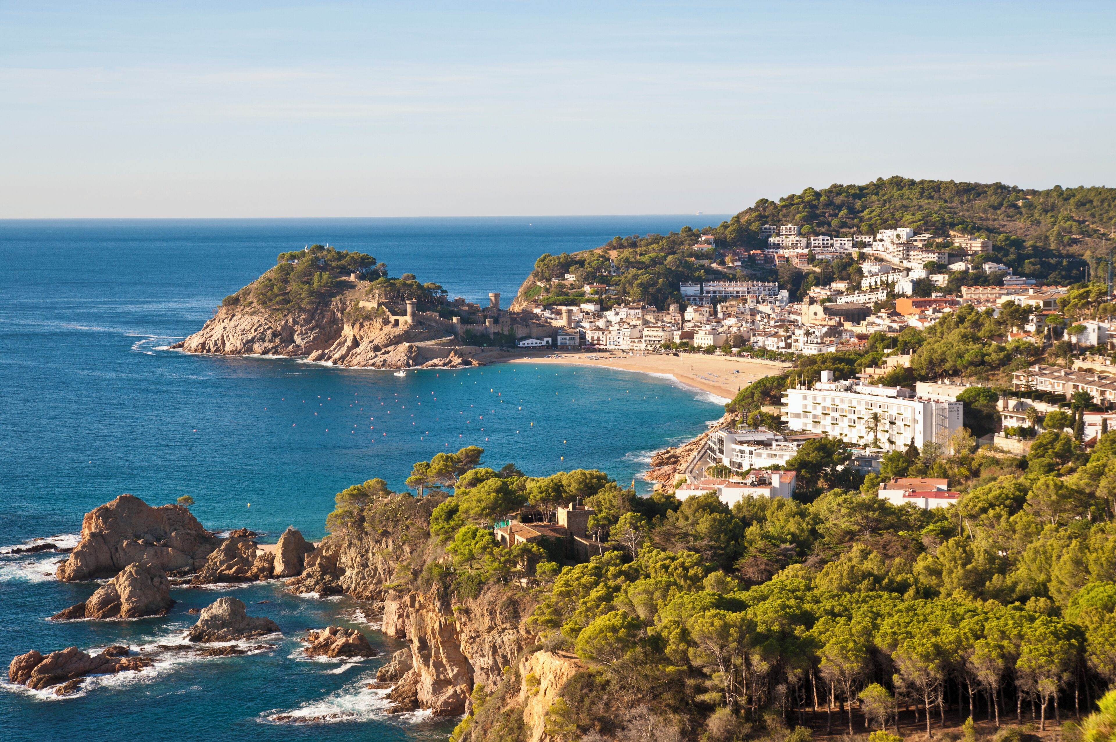 Un pueblo costero con playa, acantilados rocosos y una colina con edificios.