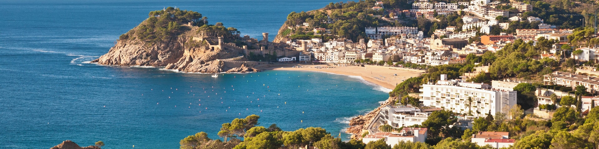 Un pueblo costero con playa, acantilados rocosos y una colina con edificios.