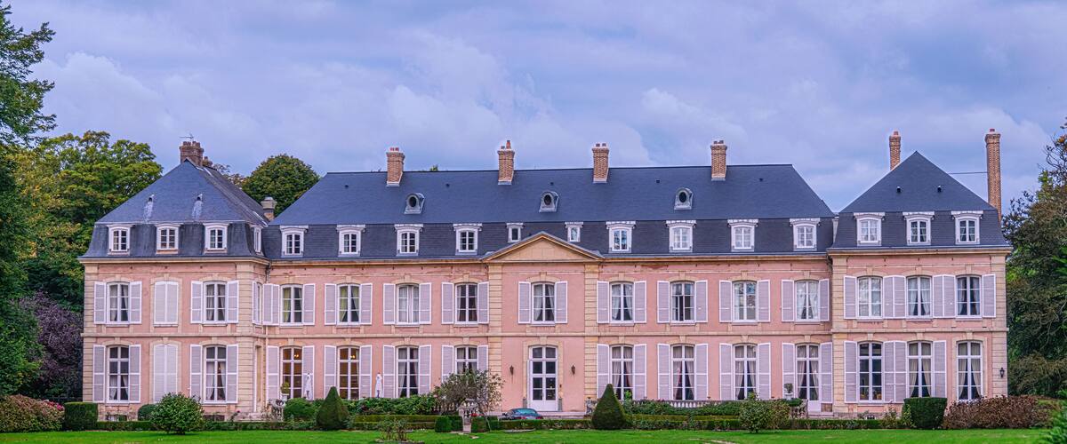 A large, multi-story pink building with white shutters, surrounded by a well-maintained lawn and trees.