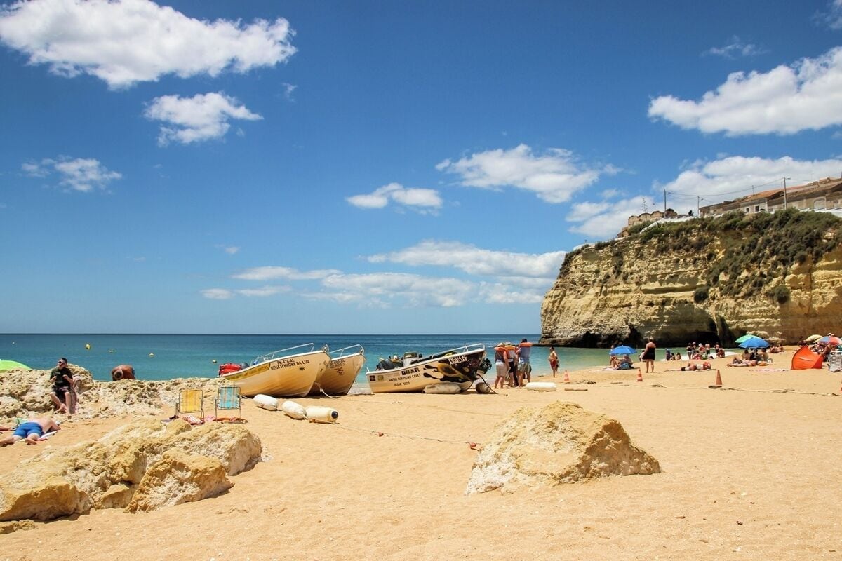 A sandy beach with boats, people, and a cliff.