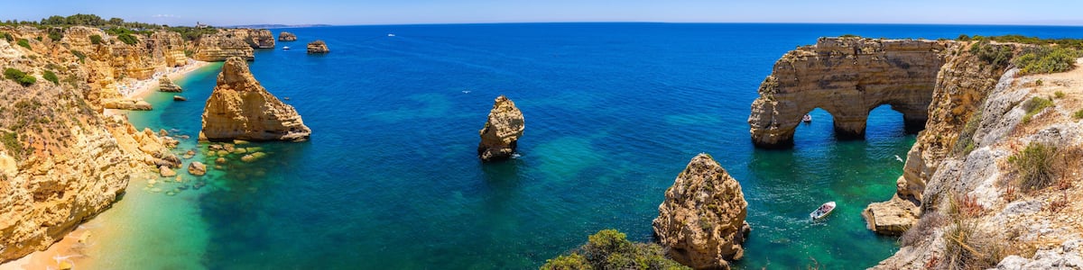 Un paysage côtier caractérisé par des eaux d’un bleu limpide, des falaises rocheuses et une grande formation rocheuse surmontée d’une arche naturelle.