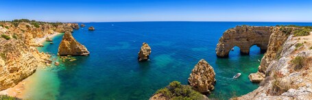 A coastal landscape with clear blue waters, rocky cliffs, and a large rock formation with an arch.