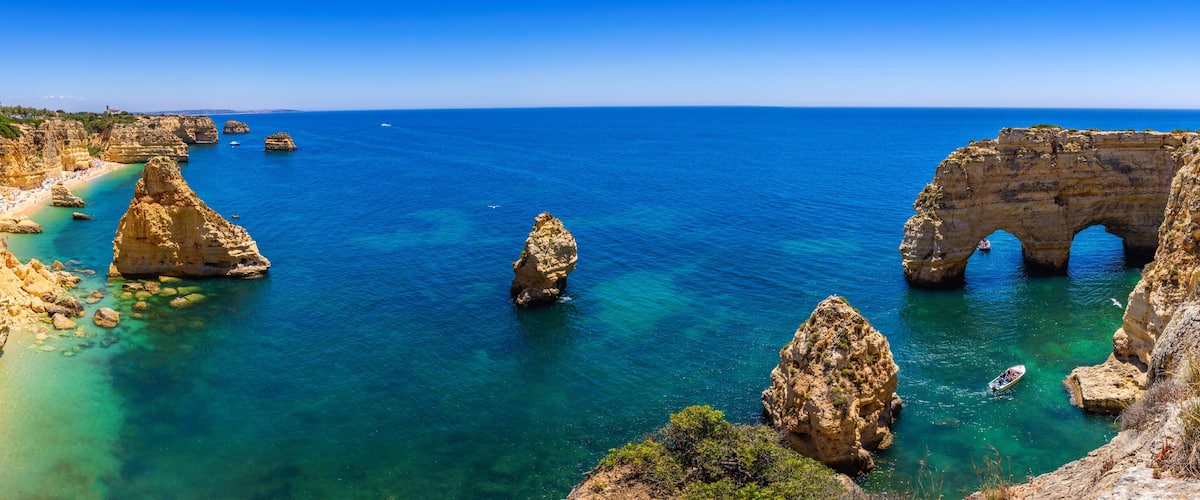 A coastal landscape with clear blue waters, rocky cliffs, and a large rock formation with an arch.