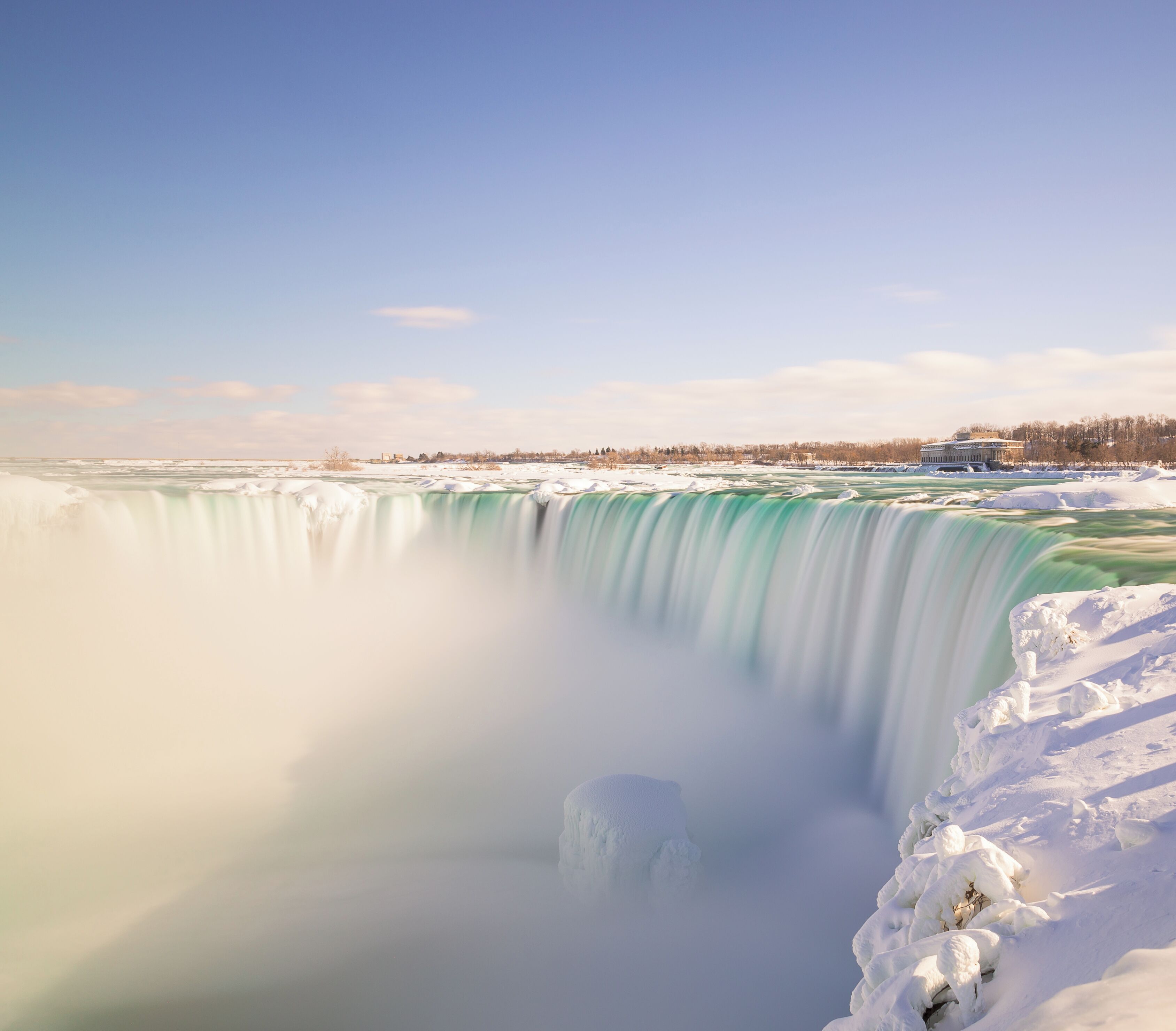 Uma grande cachoeira rodeada de neve, com um edifício ao fundo.