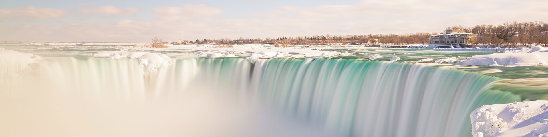 Uma grande cachoeira rodeada de neve, com um edifício ao fundo.