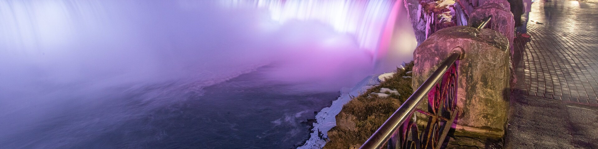 Uma cachoeira à noite, com edifícios iluminados ao fundo.