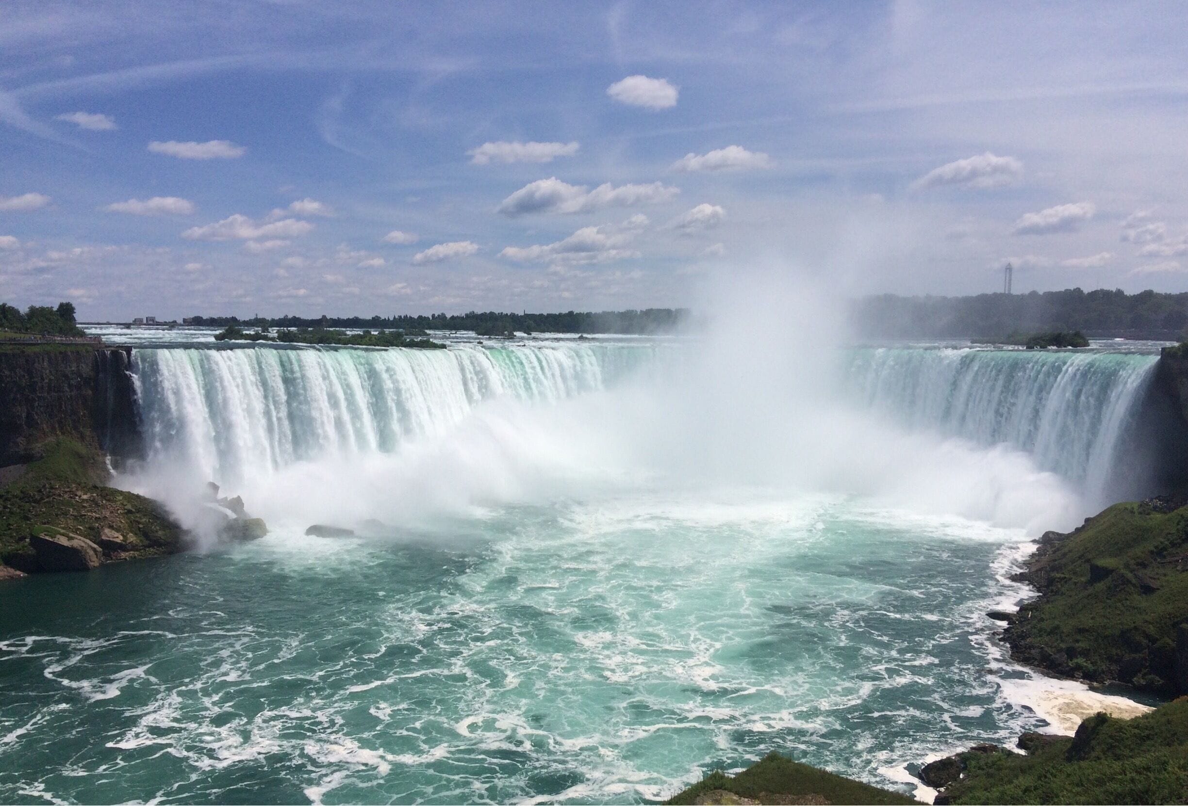 Une grande cascade dont les embruns créent une brume, entourée de verdure et sous un ciel dégagé.