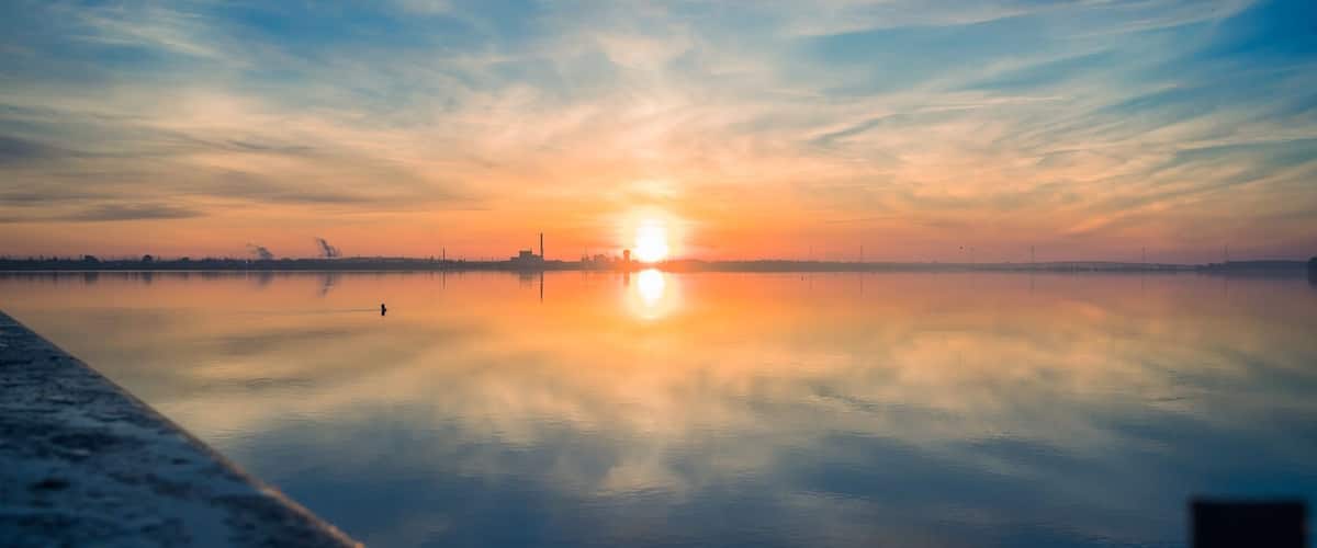 A sunset over a calm body of water with a clear sky and distant city skyline.