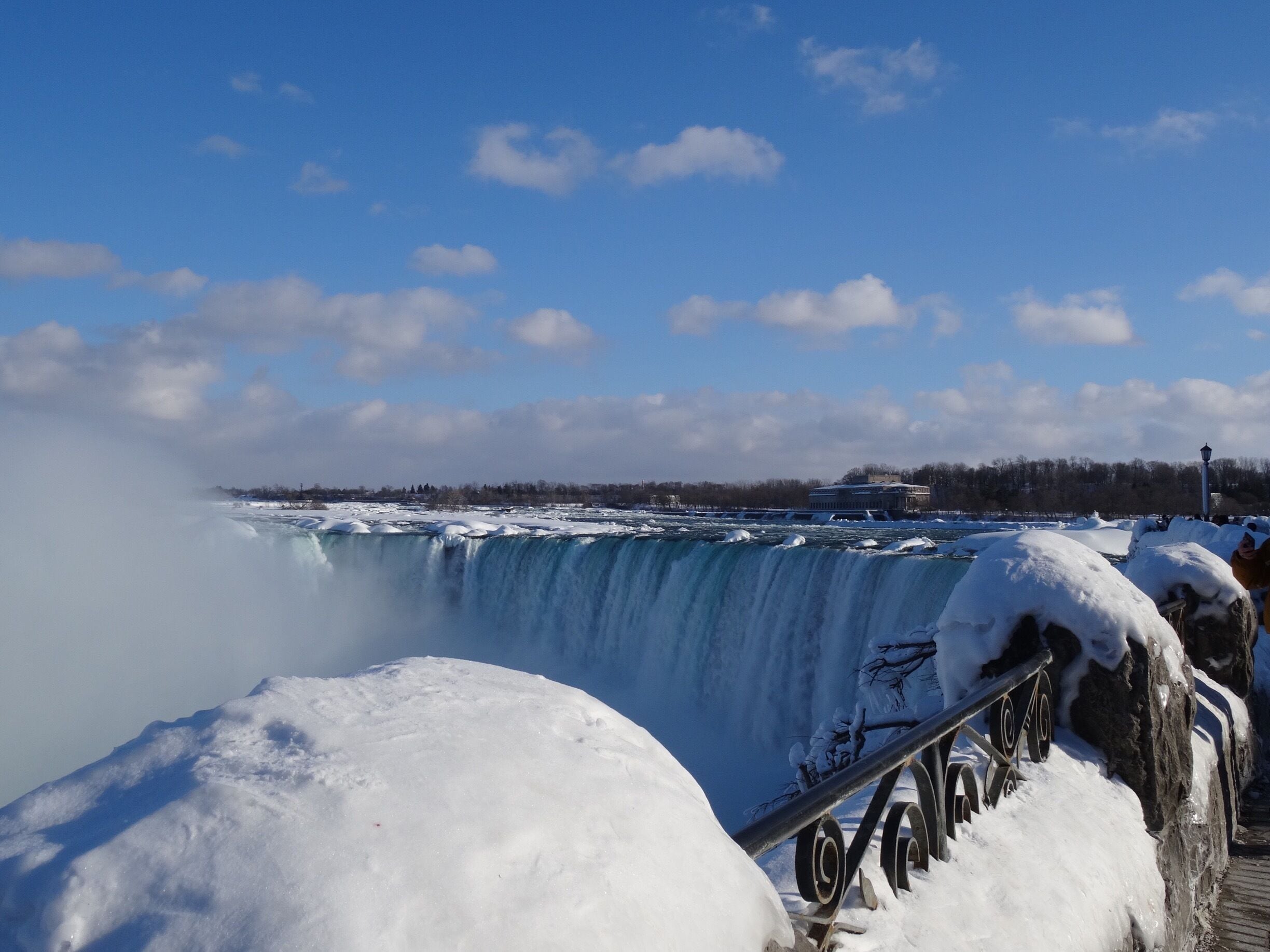 A snow-covered waterfall with a clear sky and distant buildings.