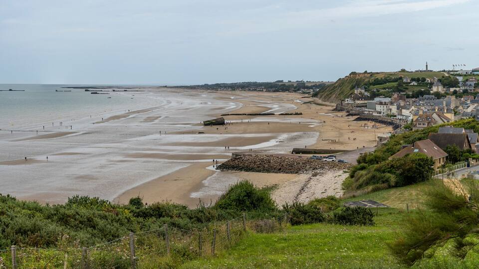 A coastal town with a sandy beach, a stone wall, and houses.