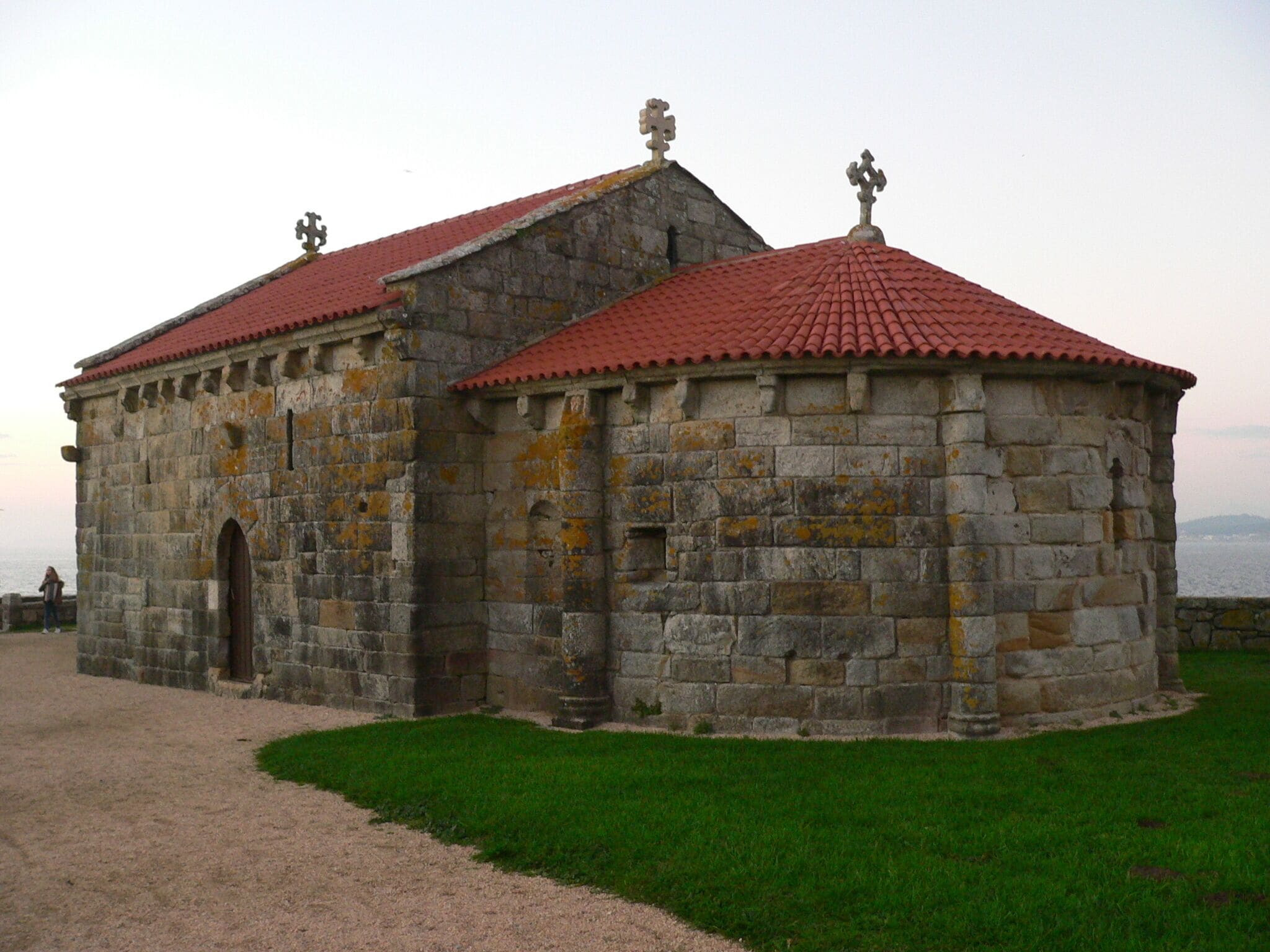 A stone building with a red-tiled roof and two crosses on top.