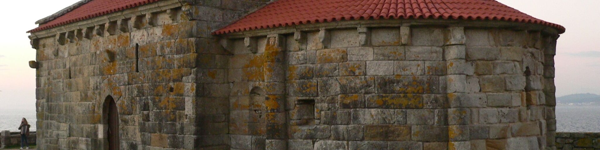 Un edificio de piedra con techo de tejas rojas y dos cruces en la parte superior.