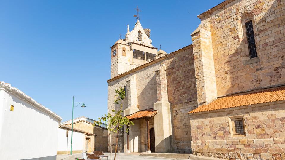 A historic church with a clock tower, stone walls, and a paved courtyard with benches.