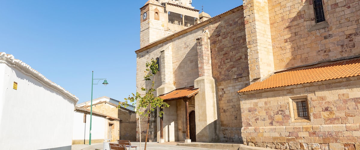 A historic church with a clock tower, stone walls, and a paved courtyard with benches.