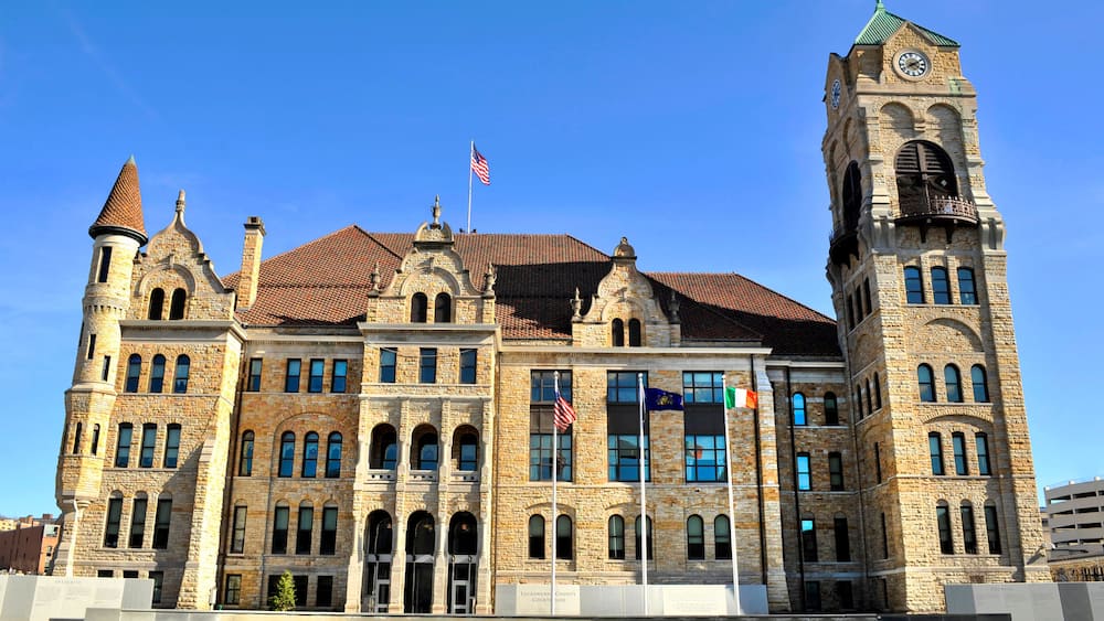 A historic courthouse with a clock tower, arched windows, and a flagpole with multiple flags.