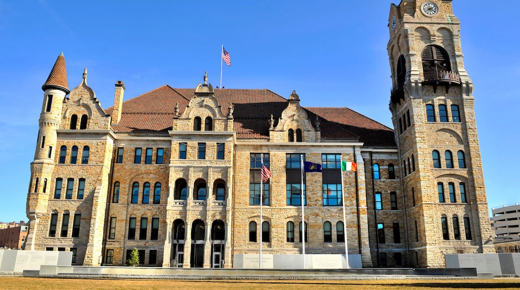 A historic courthouse with a clock tower, arched windows, and a flagpole with multiple flags.