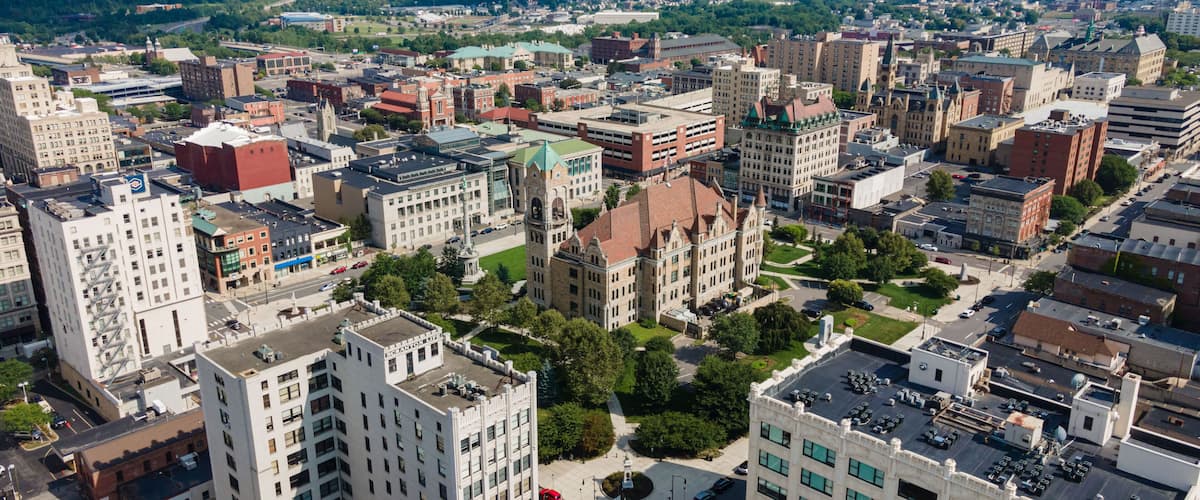 An aerial view of a city with historic architecture, green spaces, and a mountainous backdrop.