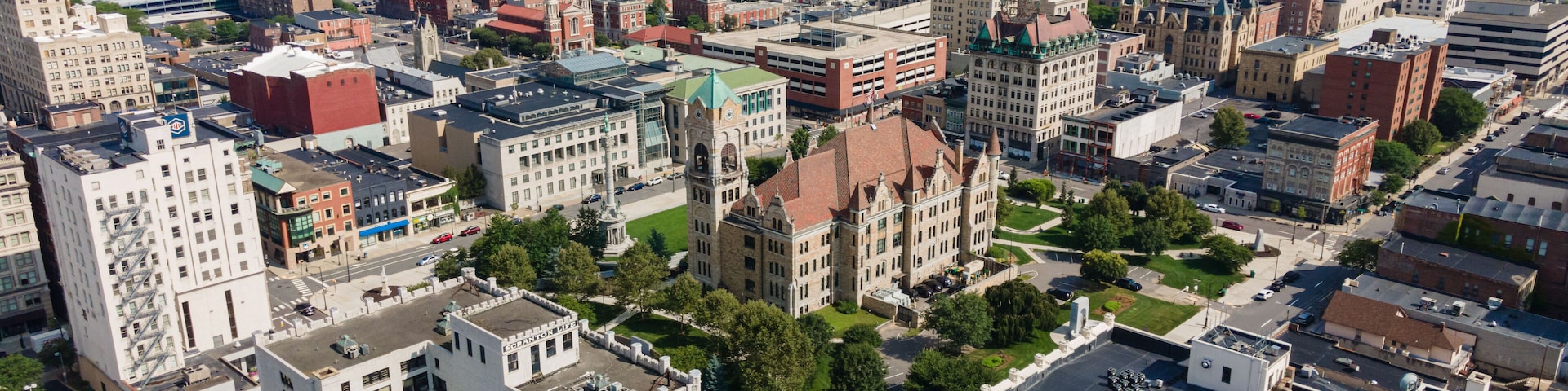 An aerial view of a city with historic architecture, green spaces, and a mountainous backdrop.