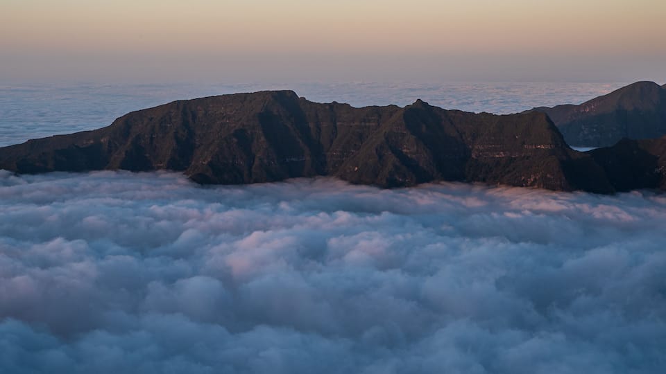 A mountain range above a sea of clouds at sunrise or sunset.
