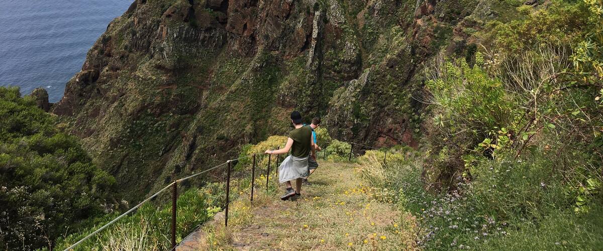 A person hiking on a rocky path with a steep cliff and ocean in the background.