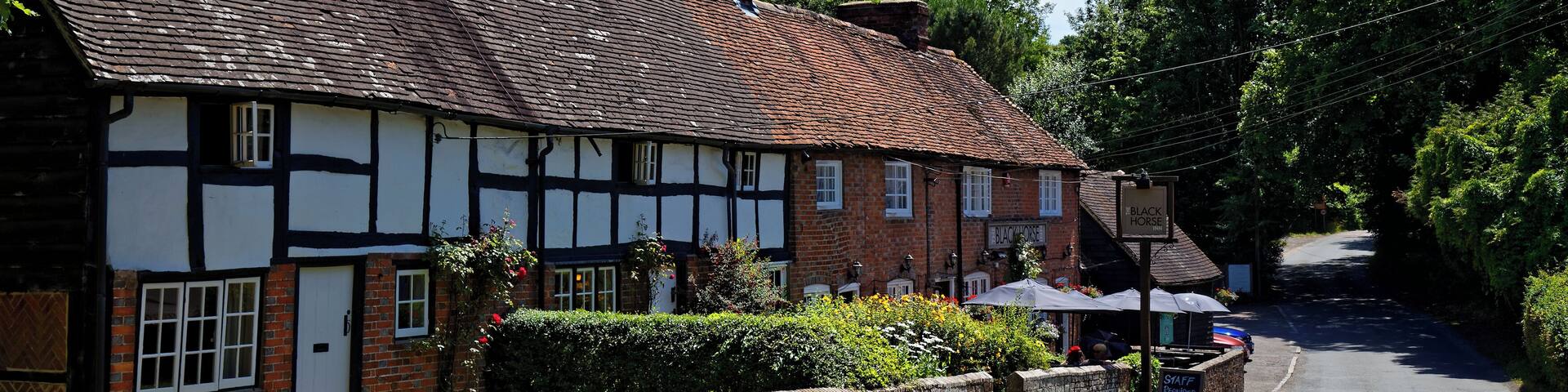 A traditional half-timbered house with a brick chimney, a stone wall, and a signboard.