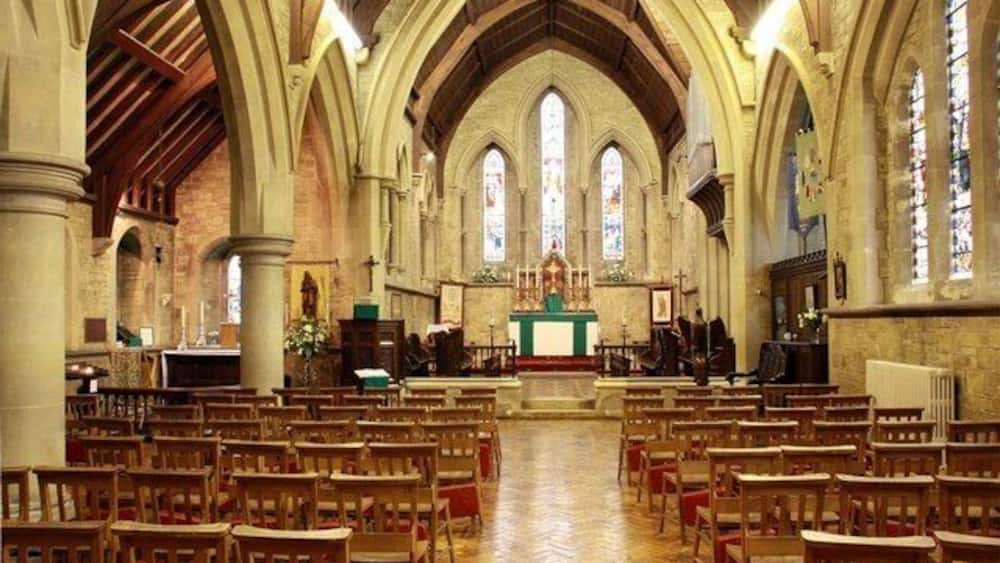 A church interior with arched ceilings, wooden pews, and stained glass windows.