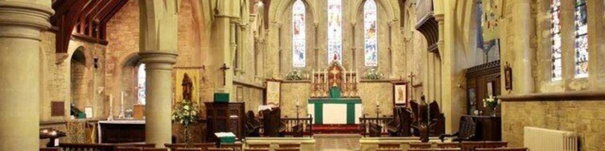 L’intérieur d’une église, avec des voûtes en arc, des bancs en bois et des vitraux.