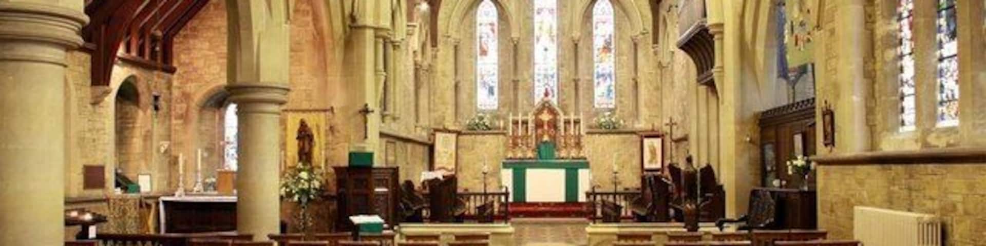 A church interior with arched ceilings, wooden pews, and stained glass windows.