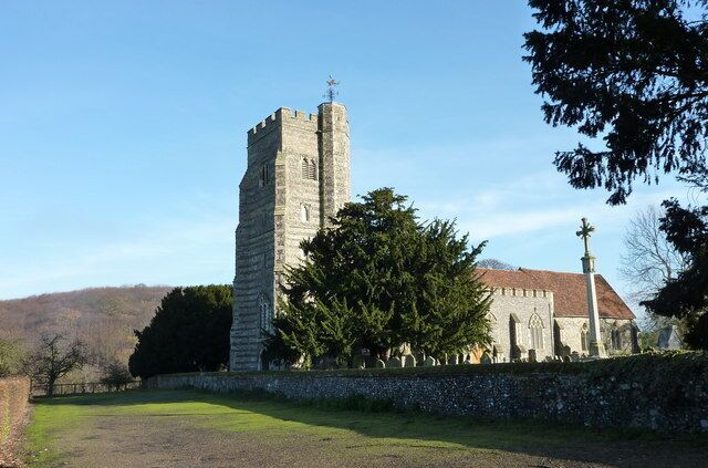 A stone church with a tall tower and a large tree in front.