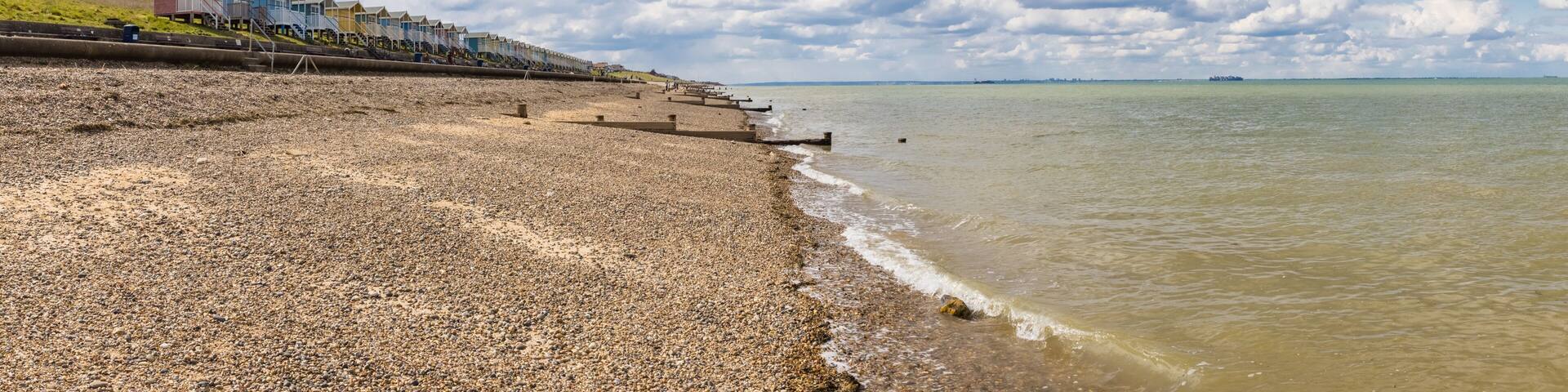 A pebbled beach with colorful seaside houses and a cloudy sky.