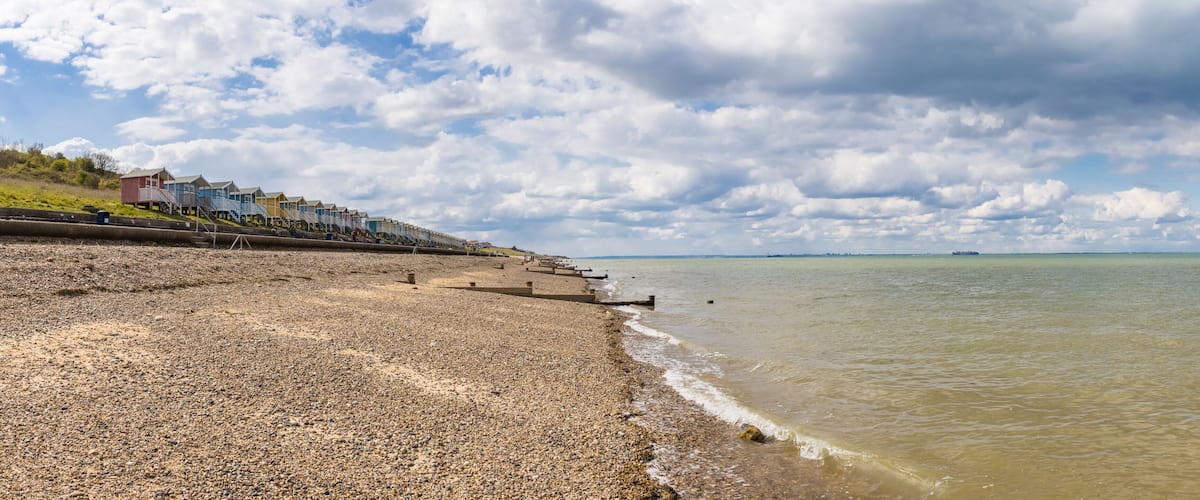 A pebbled beach with colorful seaside houses and a cloudy sky.