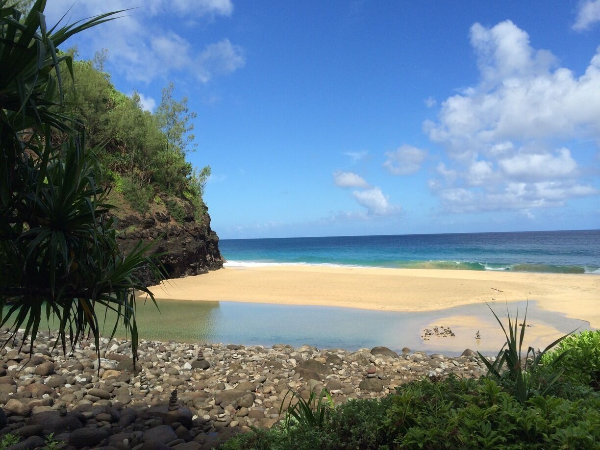 A beach with clear turquoise water, a sandy shore, and rocky foreground.