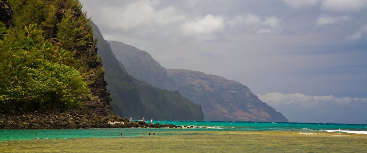 A coastal landscape with a mountain, turquoise waters, and a grassy area with people.