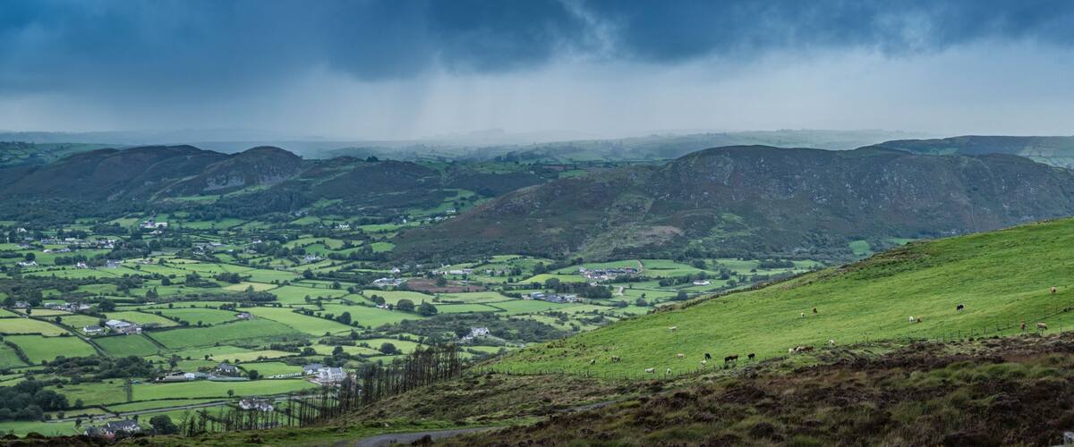 A green valley with scattered houses and rolling hills under a cloudy sky.