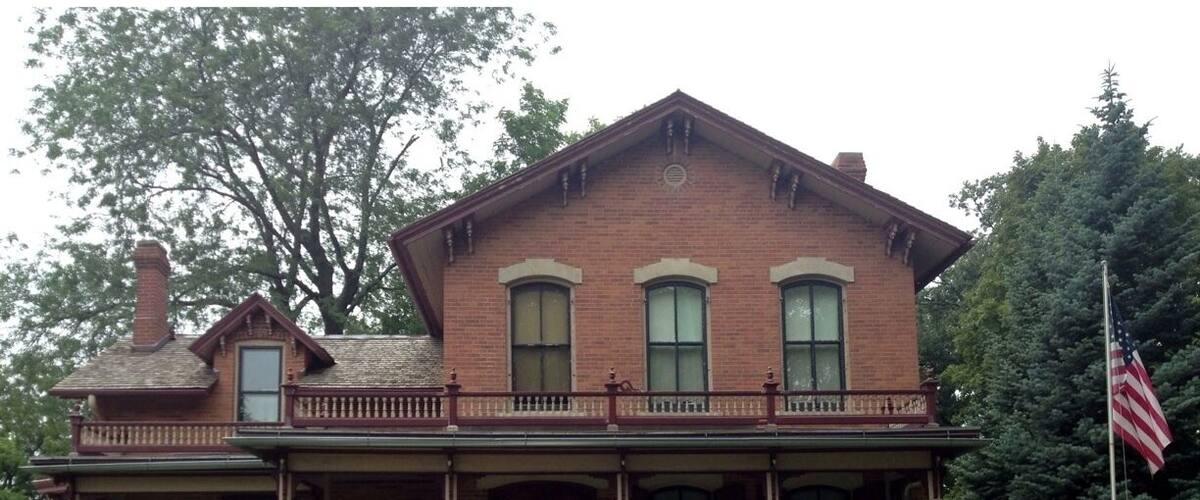A brick building with a porch, a flag, and a sign in front.