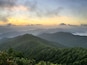Un paysage montagneux avec de vastes forêts verdoyantes, et un lever ou un coucher de soleil en arrière-plan.
