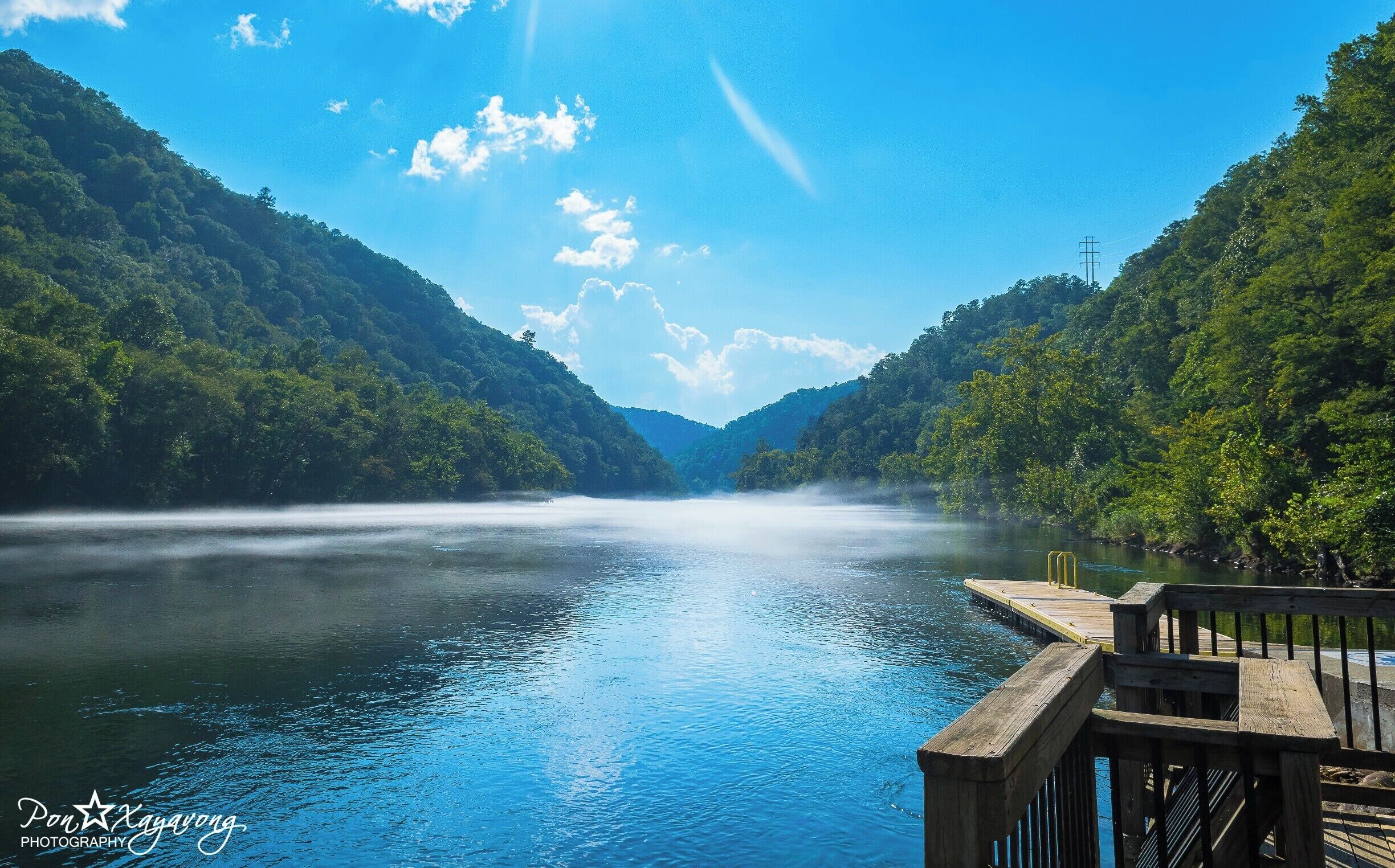 A calm river flanked by lush green hills under a clear blue sky.