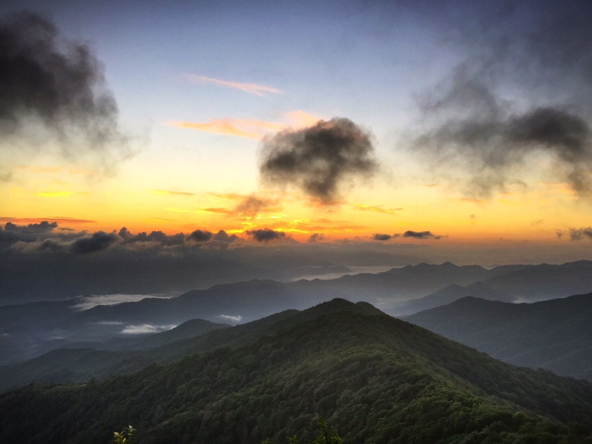 A mountain range at sunset with clouds above.
