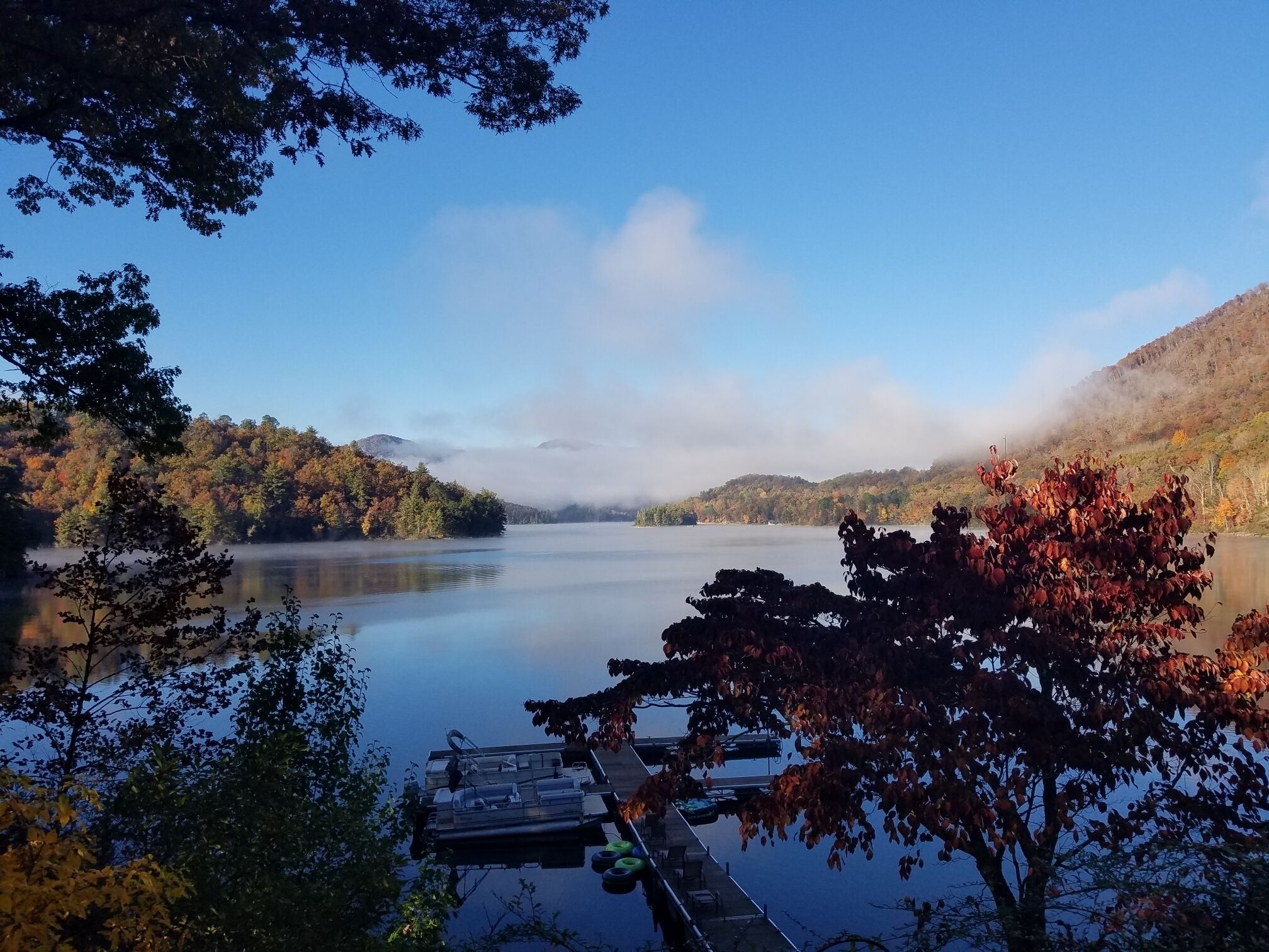 A calm lake surrounded by autumn-colored trees and a dock with boats.