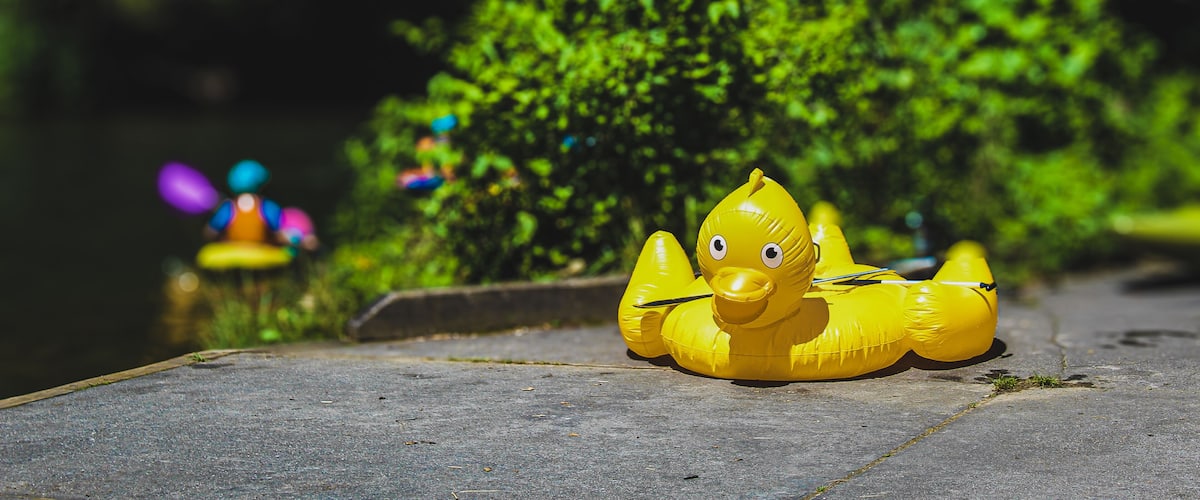 a large inflatable duck sits with a paddle on the riverside. a kayaker is blurred in the distance on the Nantahala River, flowing through the mountains of Appalachia in North Carolina. Whitewater fun.