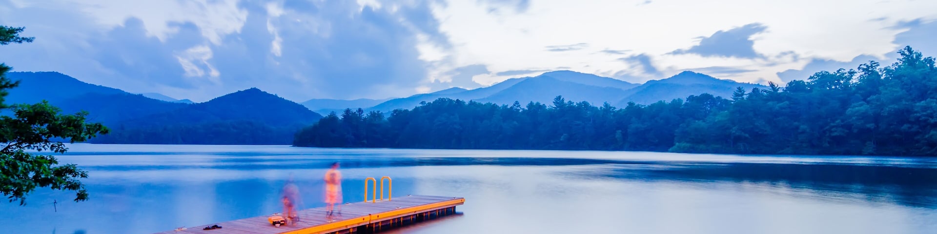 A wooden dock extending into a calm lake with mountains in the background.
