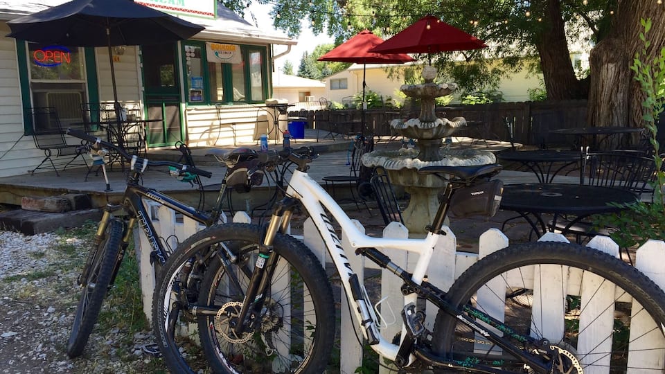 A bicycle parked near a restaurant with outdoor seating and a decorative fountain.