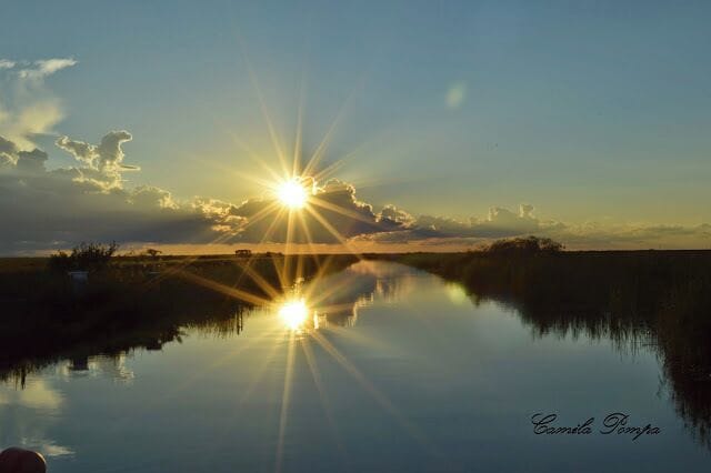 A sunset over a calm body of water with reflections of the sun and clouds.