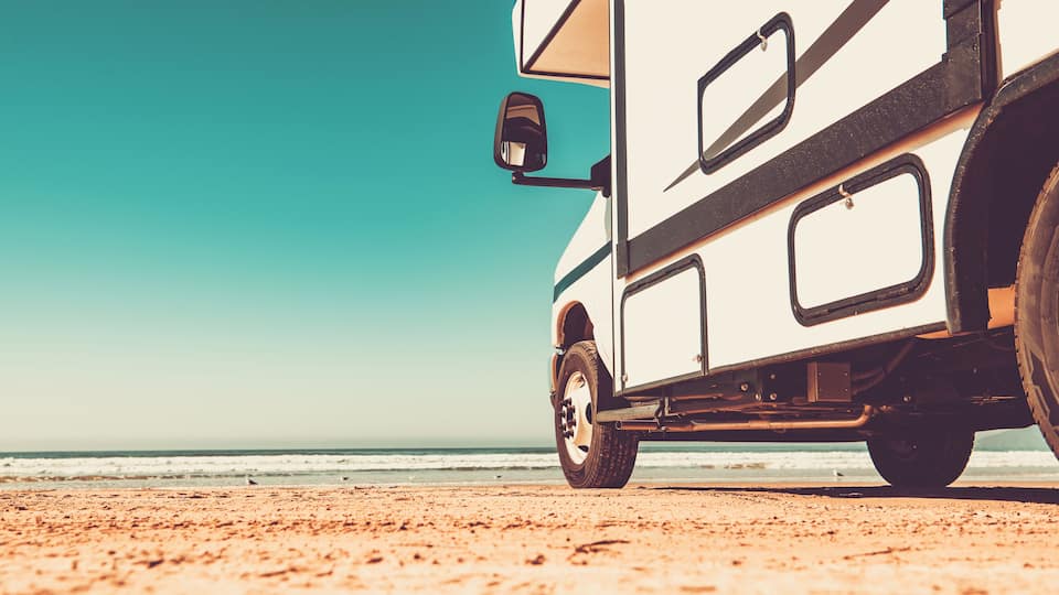 A white camper van parked on a sandy beach with the ocean in the background.