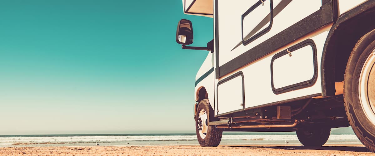 A white camper van parked on a sandy beach with the ocean in the background.