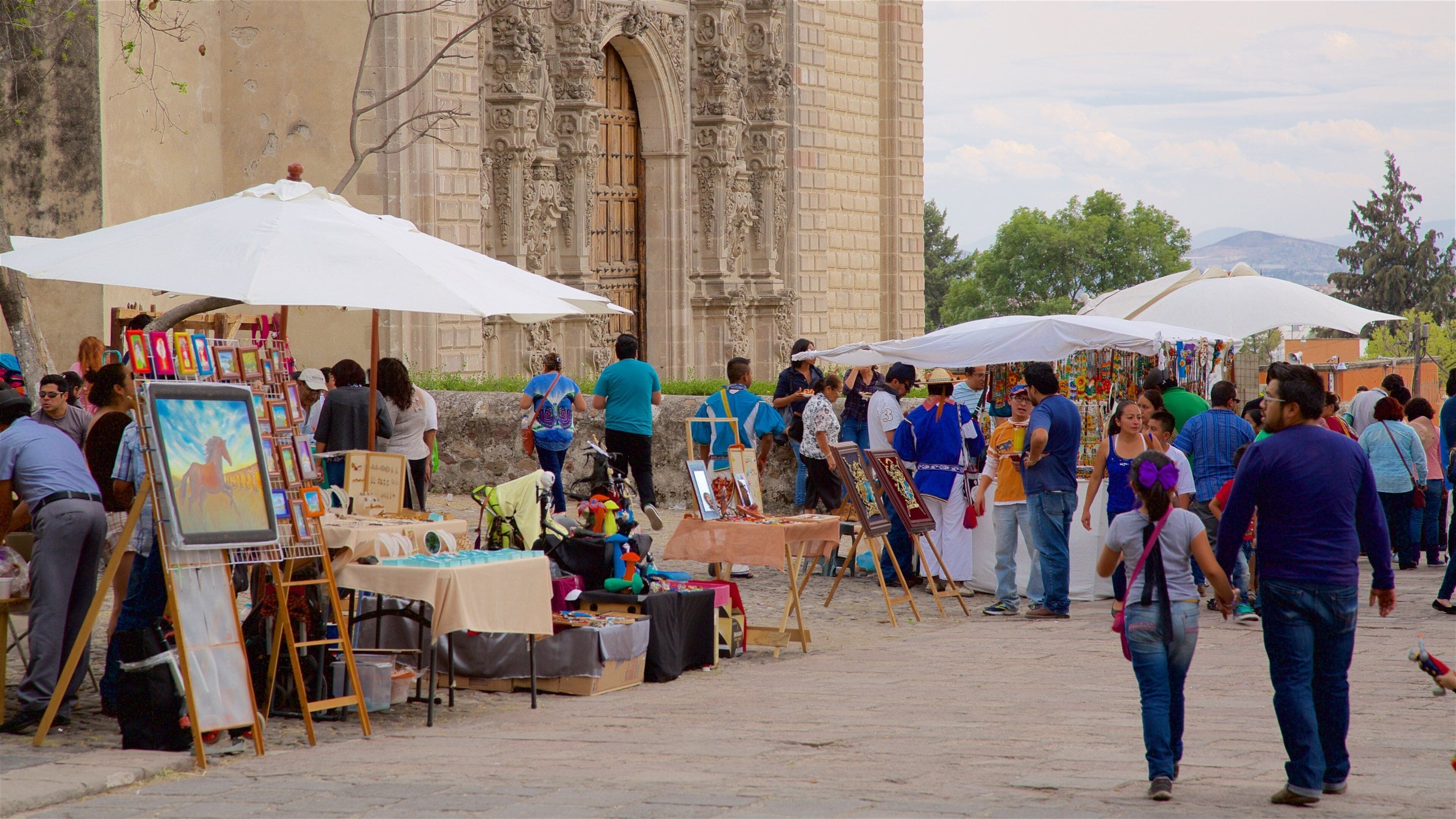 A crowded outdoor market with art stalls and a historic building in the background.