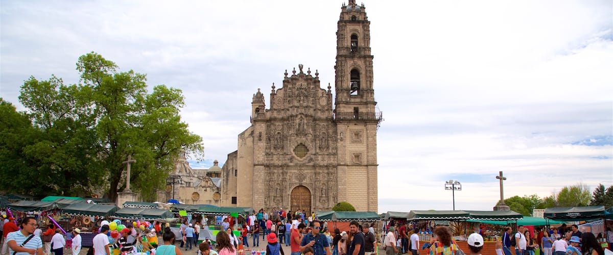 A bustling outdoor market with people and colorful stalls in front of a historic church with a bell tower.